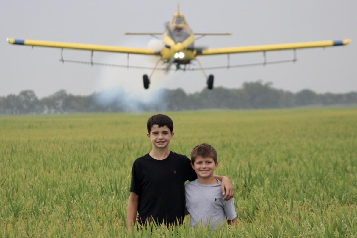 Jack & Thomas are standing in their parents rice field and their dad is flying the plane. DTH Farms